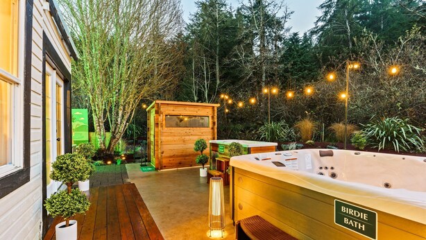 Une terrasse en bois avec un jacuzzi appelé « Bain d’oiseau », entourée de plantes en pot et d’arbres.