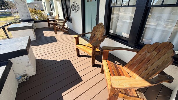 A wooden deck with Adirondack chairs and a table, a door, and windows with blinds. - Charming In-town Bungalow (Marianna)