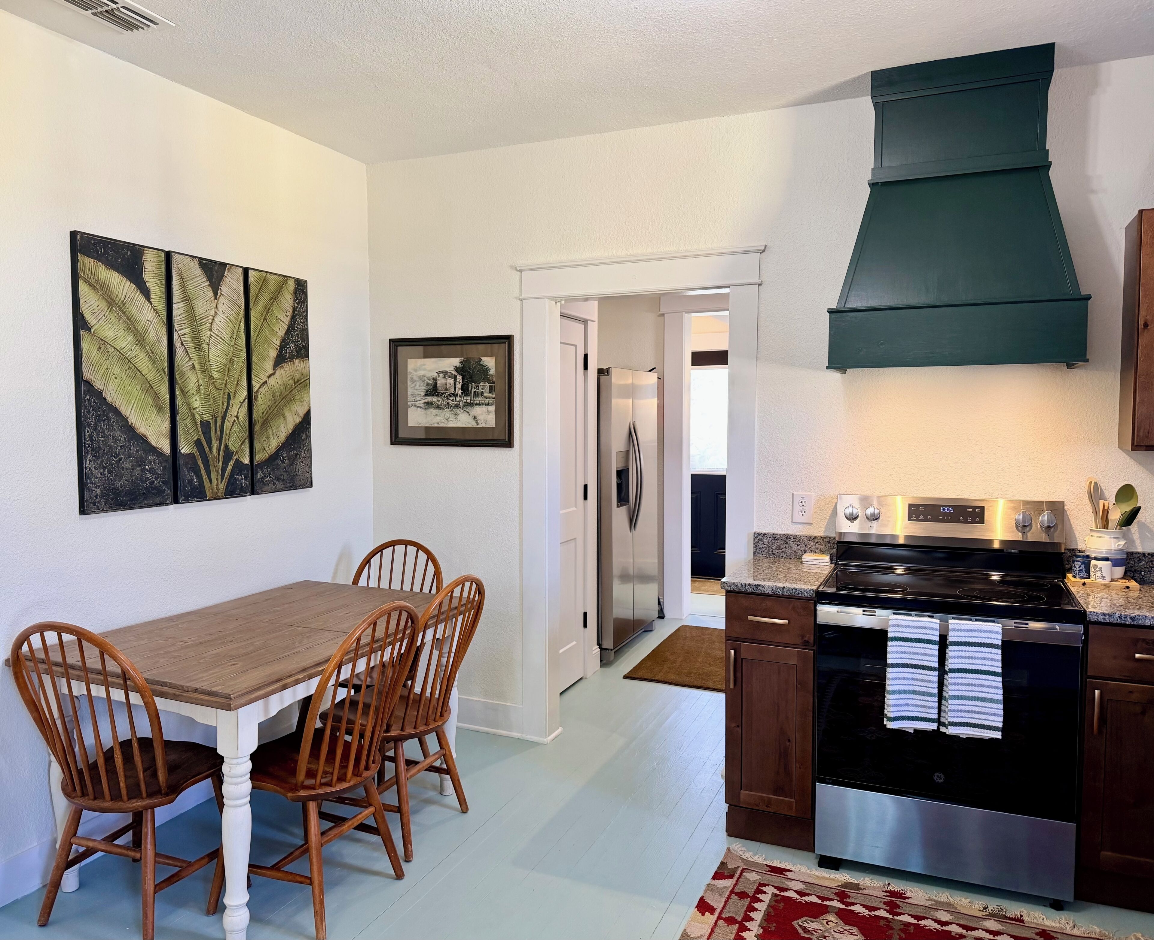 A kitchen with a stove, oven, and cabinets, a dining table with chairs, and artwork on the walls.