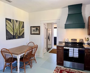 A kitchen with a stove, oven, and cabinets, a dining table with chairs, and artwork on the walls. - Charming In-town Bungalow (Marianna)