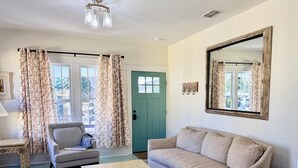 A living room with a sofa, armchair, coffee table, and a green door. - Charming In-town Bungalow (Marianna)