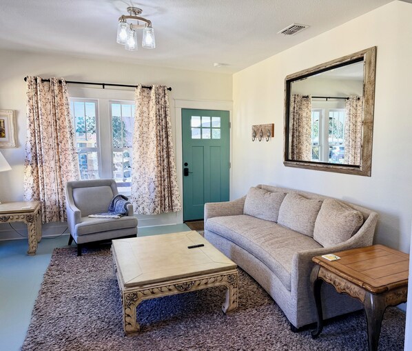 A living room with a sofa, armchair, coffee table, and a green door. - Charming In-town Bungalow (Marianna)