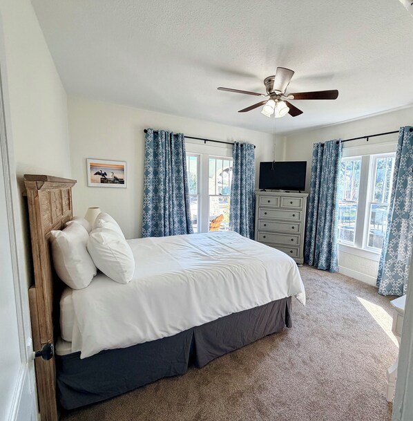 A bedroom with a bed, a ceiling fan, a dresser, and a TV.