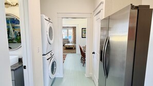 A laundry room with a washing machine and dryer, a stainless steel refrigerator, and a brown rug on the floor. - Charming In-town Bungalow (Marianna)