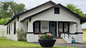 A single-story building with a gabled roof, a front porch with a bench, and a large planter with flowers. - Charming In-town Bungalow (Marianna)