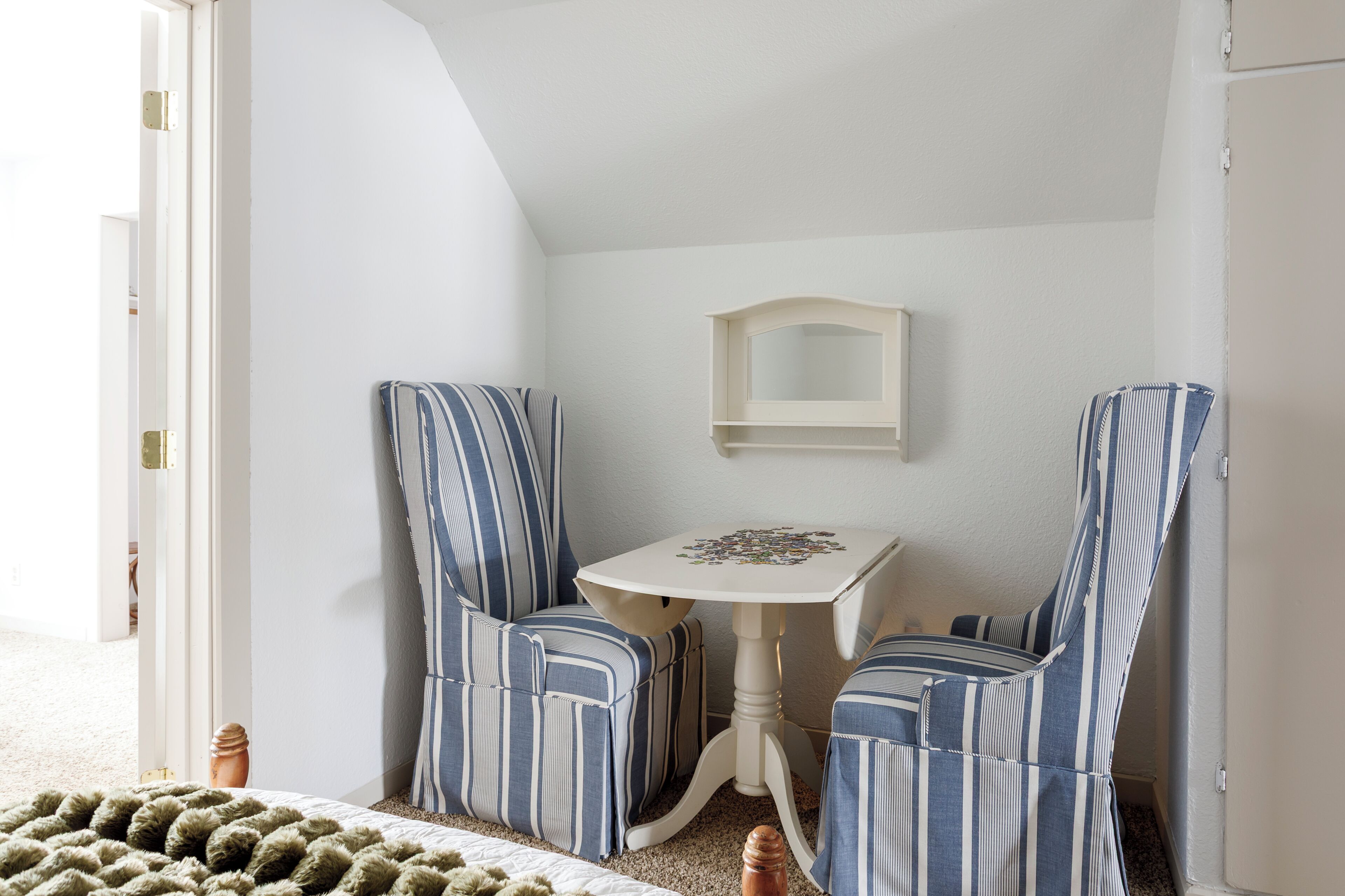 Une pièce avec deux chaises à rayures, une petite table et un miroir au mur.