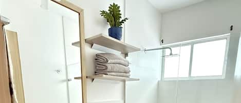 Ein modernes Badezimmer mit Waschbecken, Spiegel und Toilette. Es gibt eine Dusche mit Glastür sowie eine kleine Topfpflanze auf einem Regal.