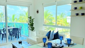 A bright, spacious living area with a glass dining table, white furniture, and large windows offering a view of palm trees. - Caribbean Retreat, apartment 304 (Cartagena)
