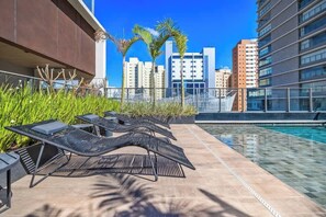 Un espace piscine aménagé sur le toit, avec des chaises longues et une vue sur les grands immeubles en arrière-plan.