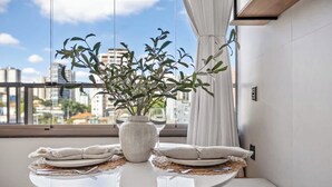 Un comedor con una mesa redonda, platos blancos y un jarrón con plantas.