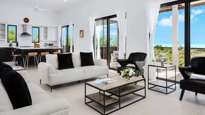 Ein modernes Wohnzimmer mit einem weißen Sofa, schwarzen Sesseln, einem Couchtisch und einer Küche im Hintergrund.