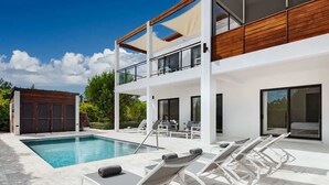 Ein modernes, zweistöckiges Haus mit Swimmingpool, Liegestühlen und einer Holzterrasse.