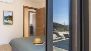 A bedroom with a bed, a door leading to a balcony, and a view of a pool and chairs.