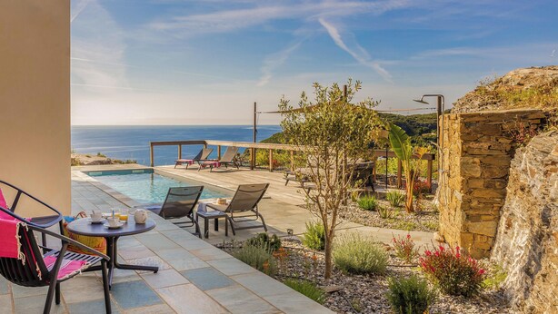 A poolside area with lounge chairs, a table with drinks, and a view of the sea.