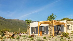 A modern building with a wooden pergola, outdoor seating, and a view of mountains.