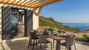 A dining area with a table set for two, overlooking a coastal landscape.