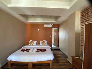 Una habitación de hotel con una cama grande, un banco de madera, un pequeño aparador de madera y una pared de ladrillo.