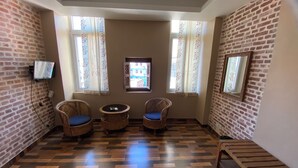 Une pièce aux murs en briques, avec deux fauteuils en osier dotés de coussins bleus, une petite table ronde et un téléviseur fixé au mur.