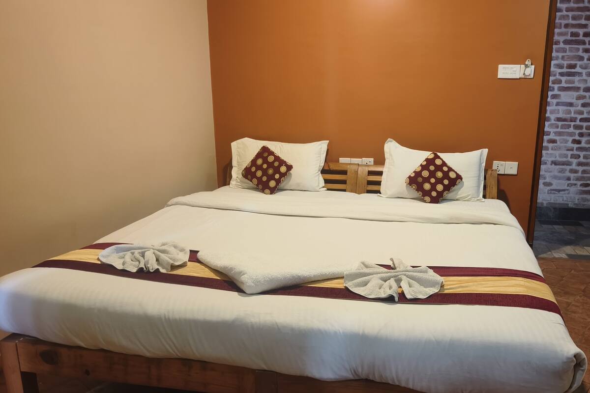 Una cama bien tendida con ropa de cama blanca, dos almohadas decorativas, un cabecero de madera y una manta a rayas.