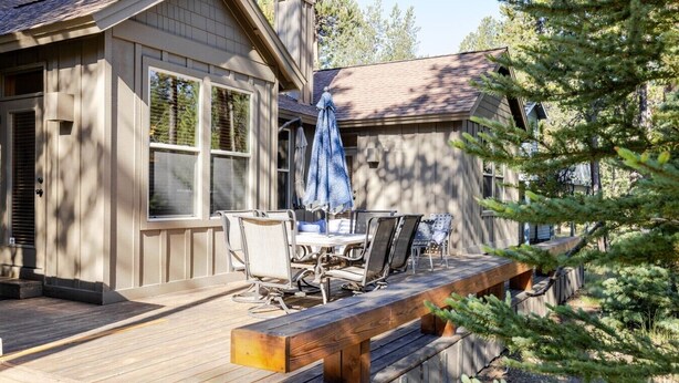 A wooden deck with outdoor furniture, a covered seating area, and a house with large windows and a chimney. - Spacious Sunriver Getaway with Hot Tub and Games (Bend)