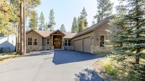 A building with a stone foundation, a garage, and a driveway leading to a wooden front door. - Spacious Sunriver Getaway with Hot Tub and Games (Bend)