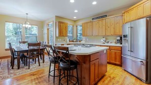 A modern kitchen with wooden cabinets, a stainless steel refrigerator, and a dining area with a table and chairs. - Spacious Sunriver Getaway with Hot Tub and Games (Bend)