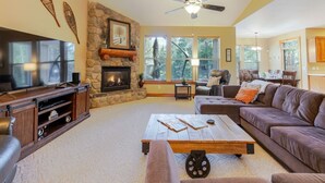 A living room with a stone fireplace, a television, a sofa, and a coffee table. - Spacious Sunriver Getaway with Hot Tub and Games (Bend)