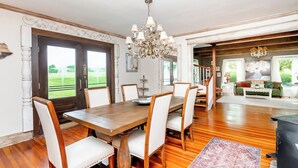 Un coin repas avec une table et des chaises en bois, un lustre et une vue sur une pelouse verdoyante, visible à travers une porte vitrée.