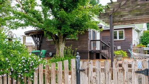 Une maison en bois avec une terrasse, un arbre et une clôture.
