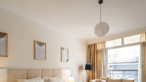 A bedroom with a large bed, a bedside table, a floor lamp, a sofa, and a window with curtains.