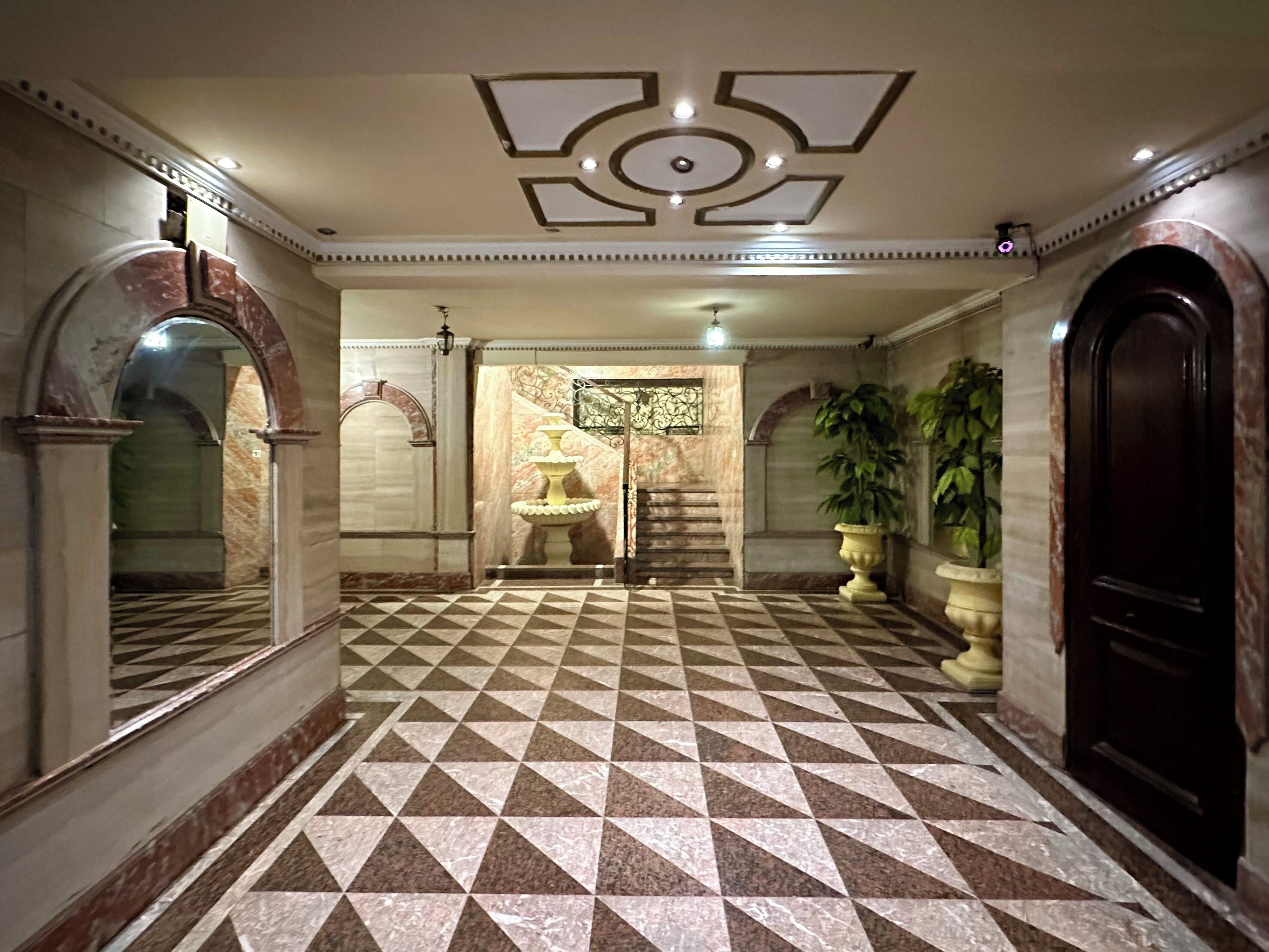 A lobby with a checkered floor, a fountain, and a staircase leading to another area.
