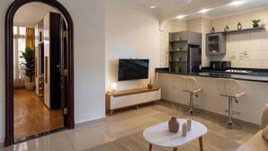 A modern kitchen with a flat-screen TV, a wooden bench, and two bar stools.