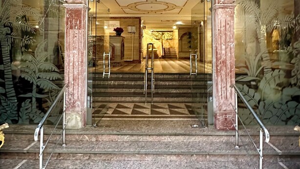 A grand entrance with a marble archway, a staircase leading up, and a glass facade reflecting the interior.