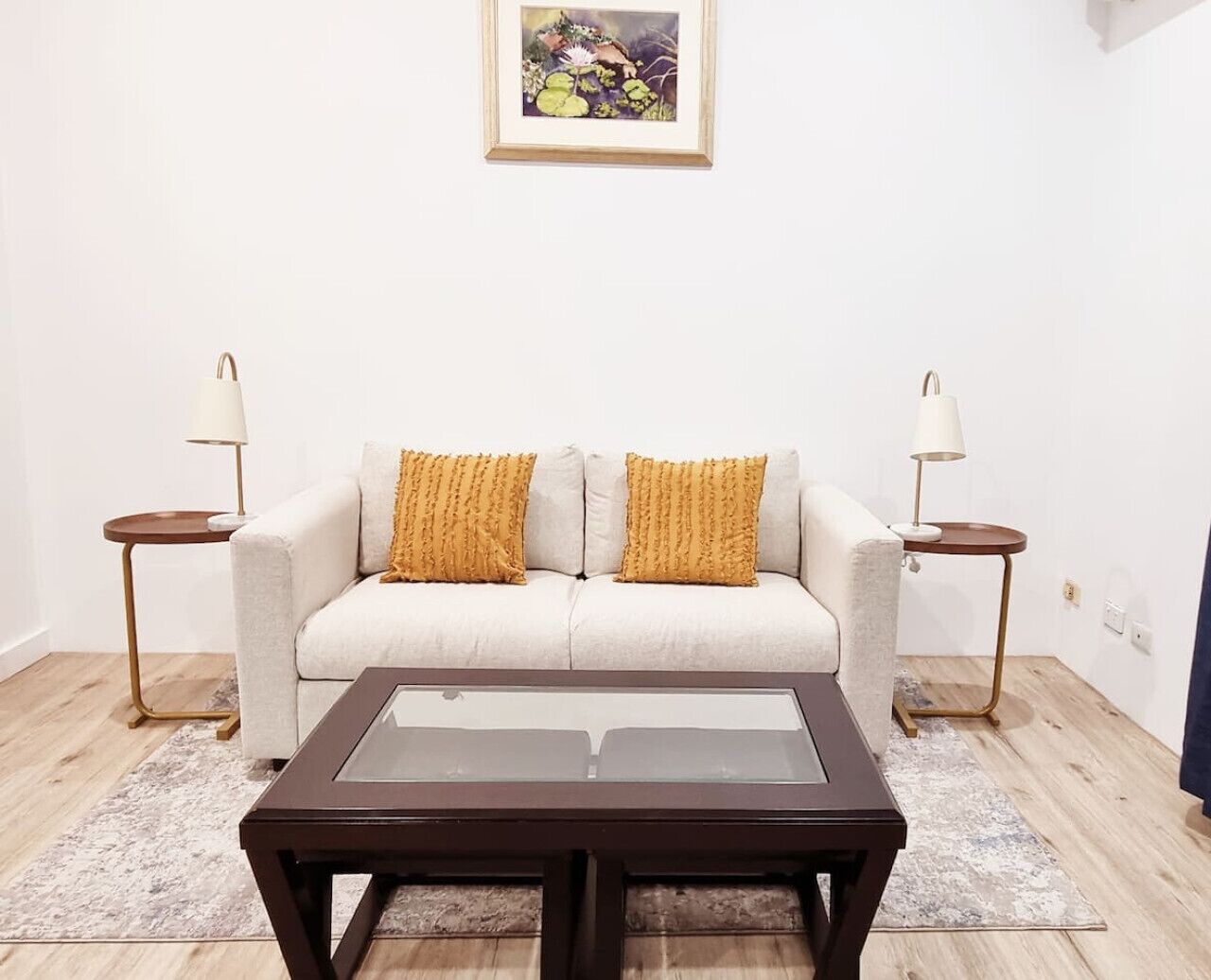 Ein Wohnzimmer mit einer Couch, zwei Beistelltischen, einem Couchtisch und einem gerahmten Bild an der Wand.