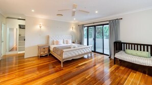 Une chambre spacieuse avec un grand lit, un plancher en bois, un ventilateur de plafond et une porte-fenêtre coulissante donnant sur un balcon.