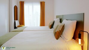 Habitación de hotel con dos camas, un espejo, una lámpara colgante y un ventanal con cortinas.