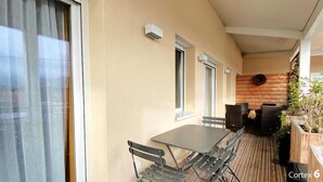 Un balcón con mesa y sillas, una pared de madera y plantas en macetas.