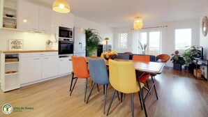 Una cocina moderna con armarios blancos, un microondas y una estufa. Hay un comedor con sillas coloridas y una mesa.
