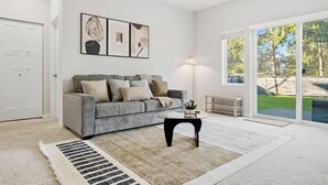 A modern living room with a grey sofa, a coffee table, and a large window offering a view of a backyard.