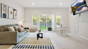 A spacious living room with a grey sofa, a coffee table, and a TV mounted on the wall.