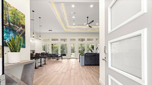A spacious, modern interior with a dining area, a seating area with a sofa, and a large window providing natural light. - Float, Relax, Repeat - Brand New 6 BR, 4.5 BA Waterfront Home On Rainbow River (Dunnellon)