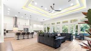 A spacious living area with a large grey sectional sofa, a wooden coffee table, and a kitchen in the background. - Float, Relax, Repeat - Brand New 6 BR, 4.5 BA Waterfront Home On Rainbow River (Dunnellon)