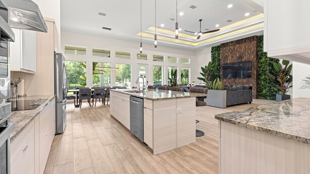 A modern kitchen with a central island, built-in appliances, and a dining area with a view of greenery. - Float, Relax, Repeat - Brand New 6 BR, 4.5 BA Waterfront Home On Rainbow River (Dunnellon)