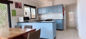 A kitchen with blue cabinets, a microwave, a gas stove, and a dining area with a wooden table and chairs.