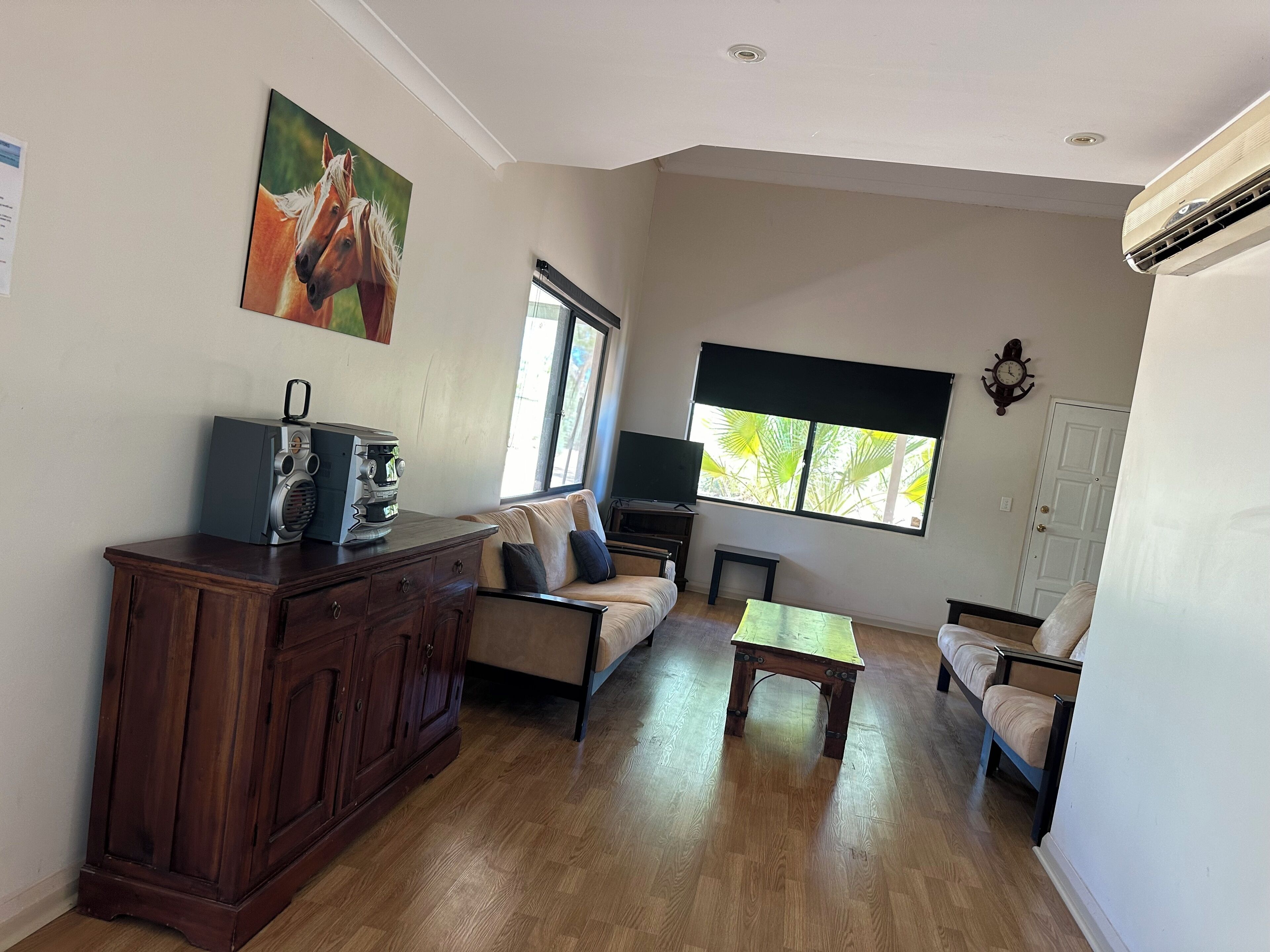 A living room with a wooden cabinet, a sofa, a coffee table, a television, and a window with a view of greenery.