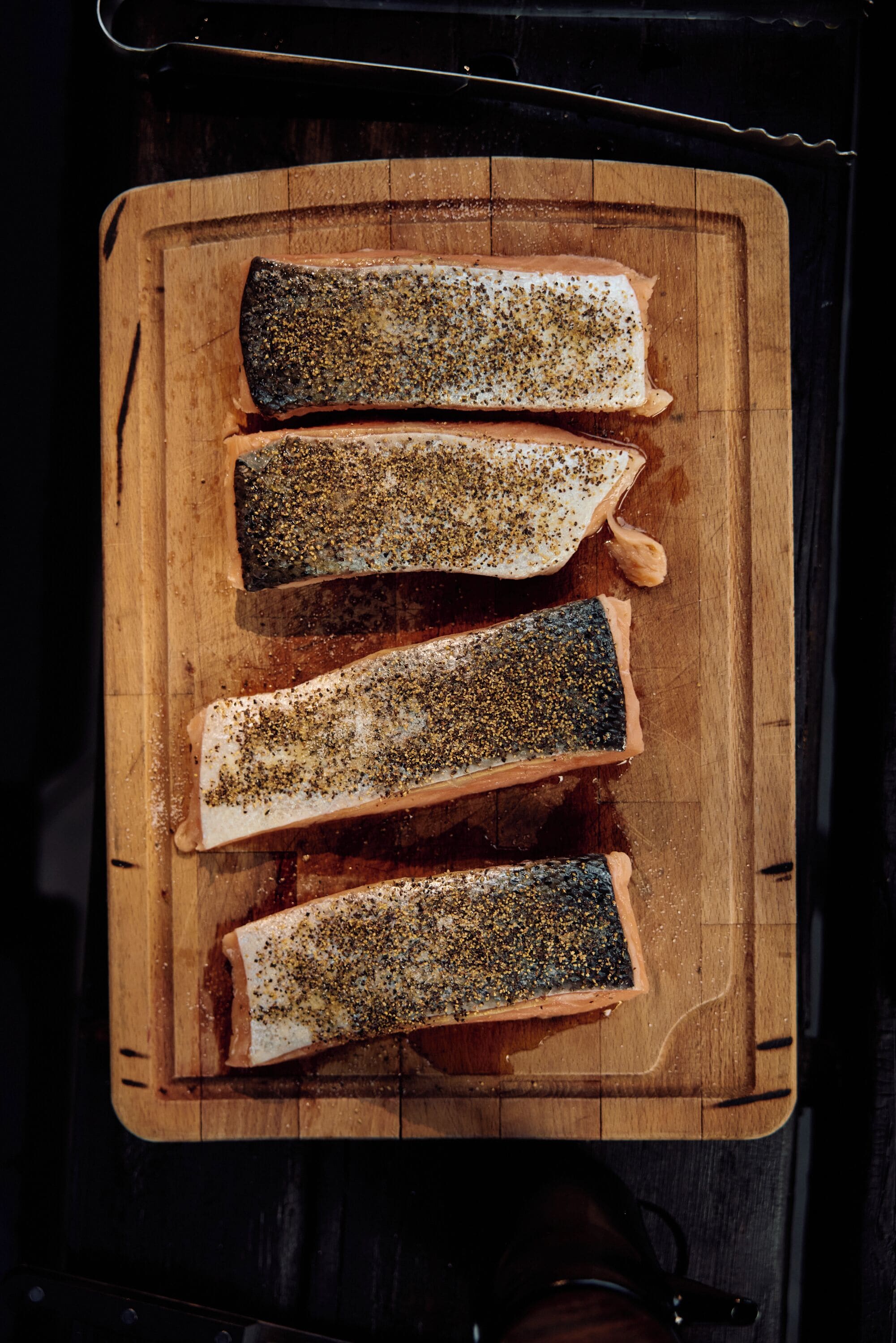 Four salmon fillets on a wooden cutting board.