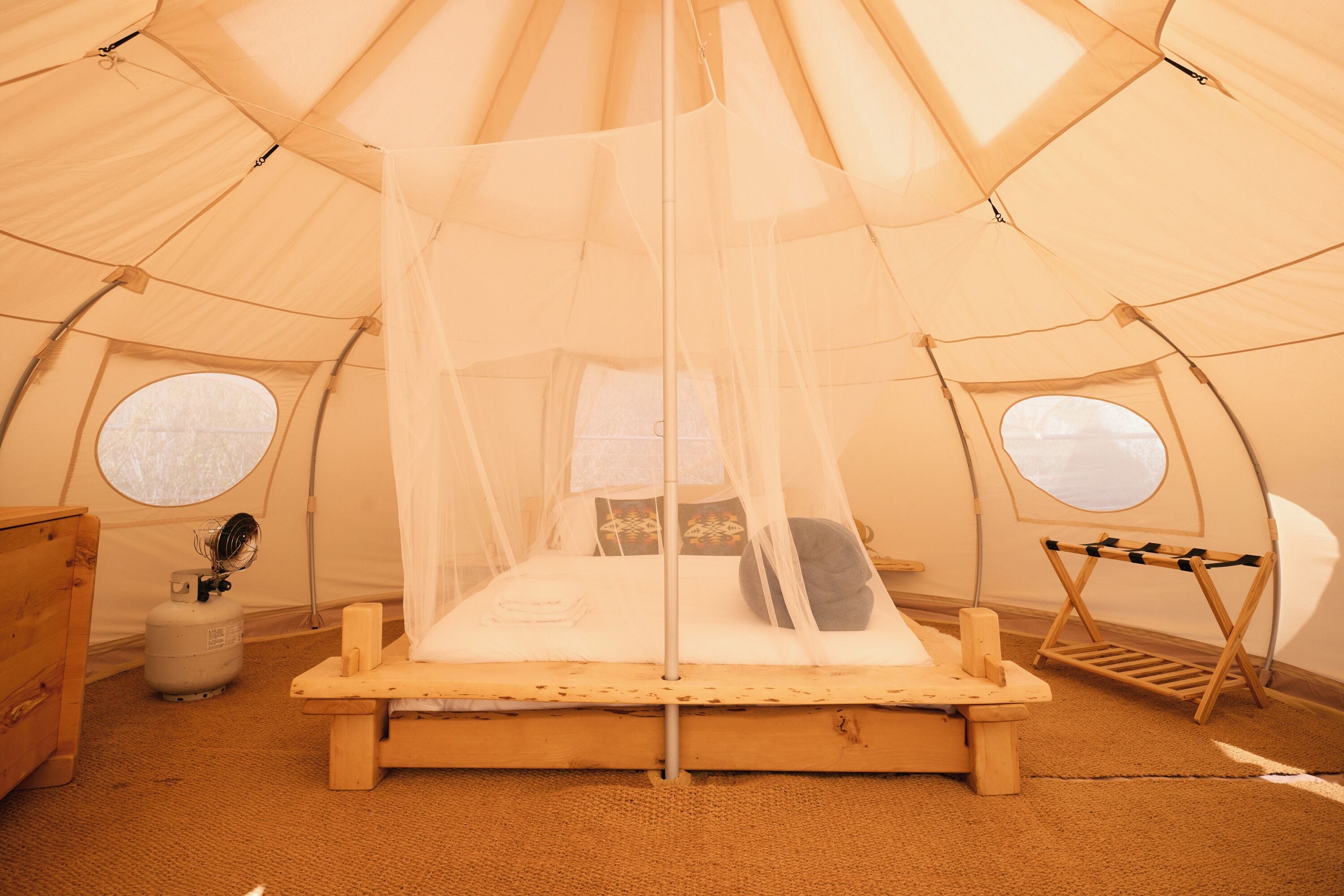 Een tent met een bed, een tafeltje en een ventilator.