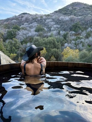 A person in a hot tub with a mountainous landscape in the background.
