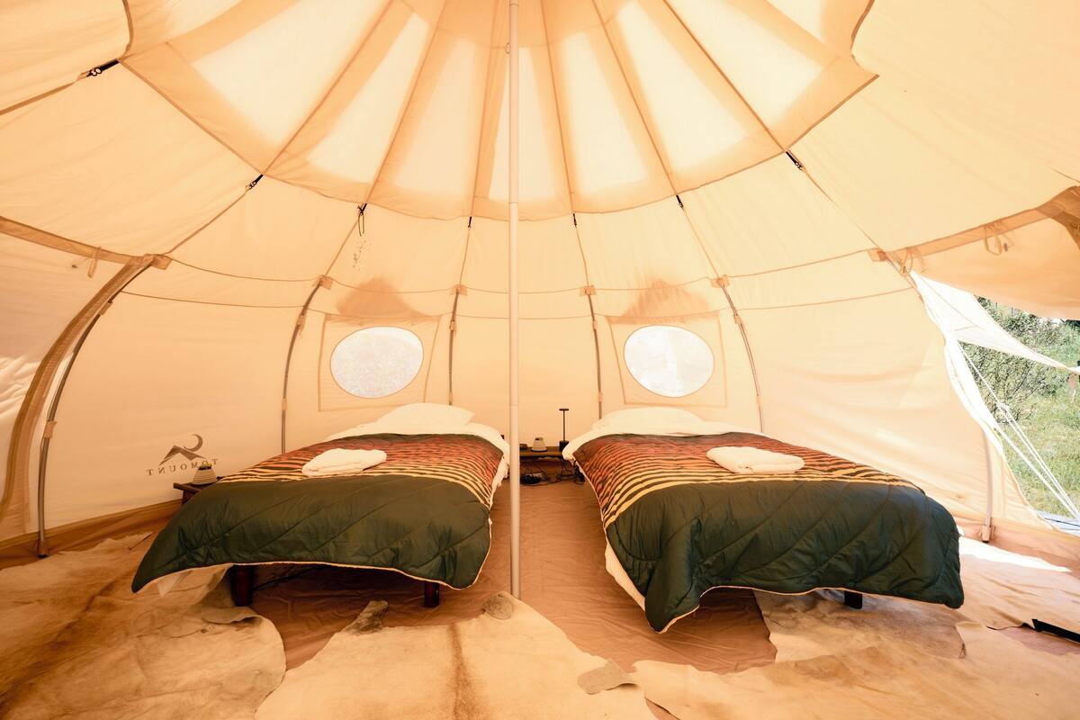 A tent with two beds, each with a pillow and a blanket.