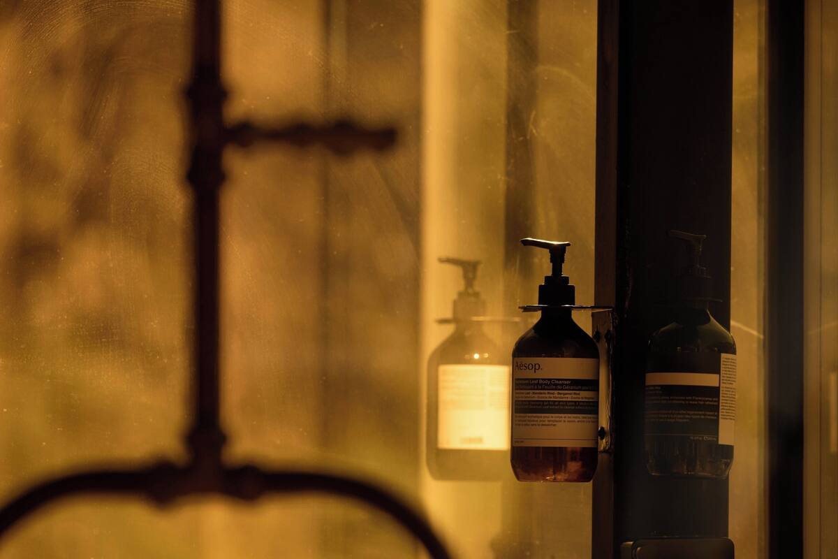 A bathroom with a mirror, a bottle of Aesop body lotion, and a bottle of liquid soap.